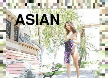 A petite Asian girl toys her shaved pussy sitting on a bench