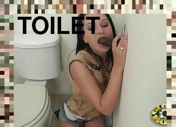 Brunette doll thrilled as she blows off a hard cock from a gloryhole in the toilet