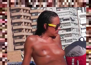 Tanned girl on a busy beach is topless