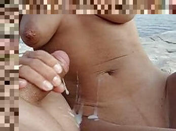 Big tittied girl gives a handjob to a guy at the beach