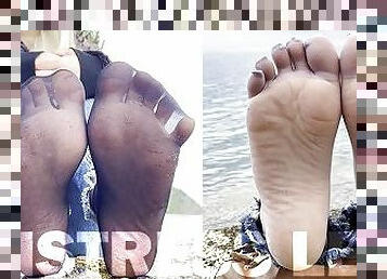 Feet tease in black and grey nylon socks wiggling toes at the seashore
