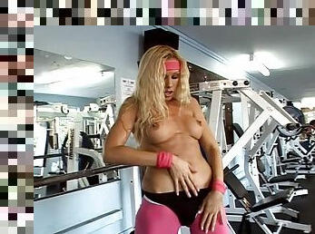 Lewd blonde Sandy plays with her shaved pussy in a gym